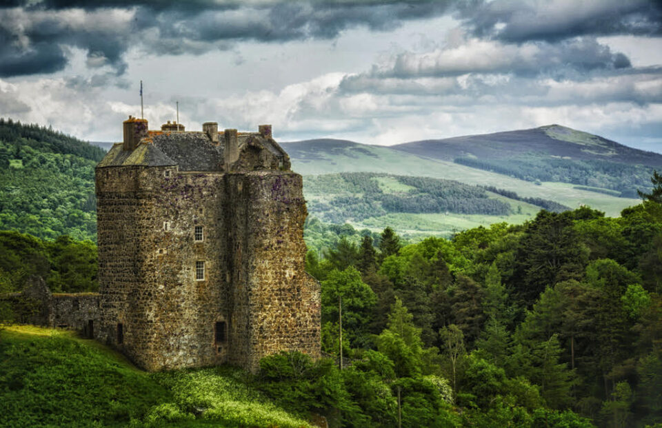 Neidpath Castle in Peebles, Scotland, United Kingdom, alongside a forest overlooking rolling green hills.